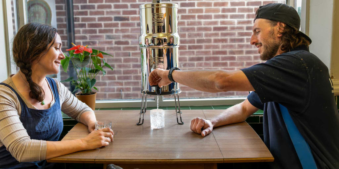 Two adults sitting at a table pouring water from gravity filter system