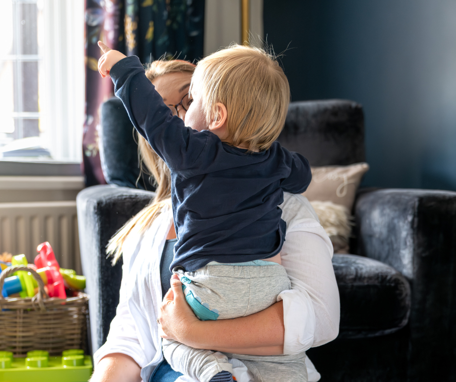 Woman holding a child in a living room with toys on the floor