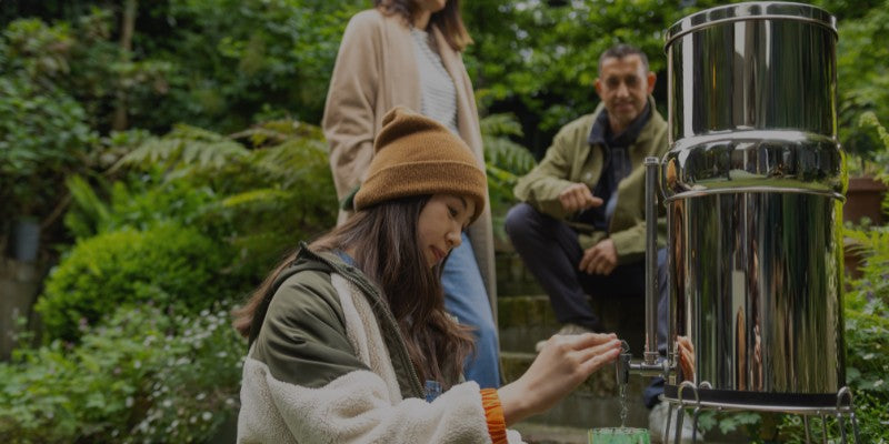 Girl outdoors pouring a glass of water from a British Berkefeld Stainless Steel Gravity System. 