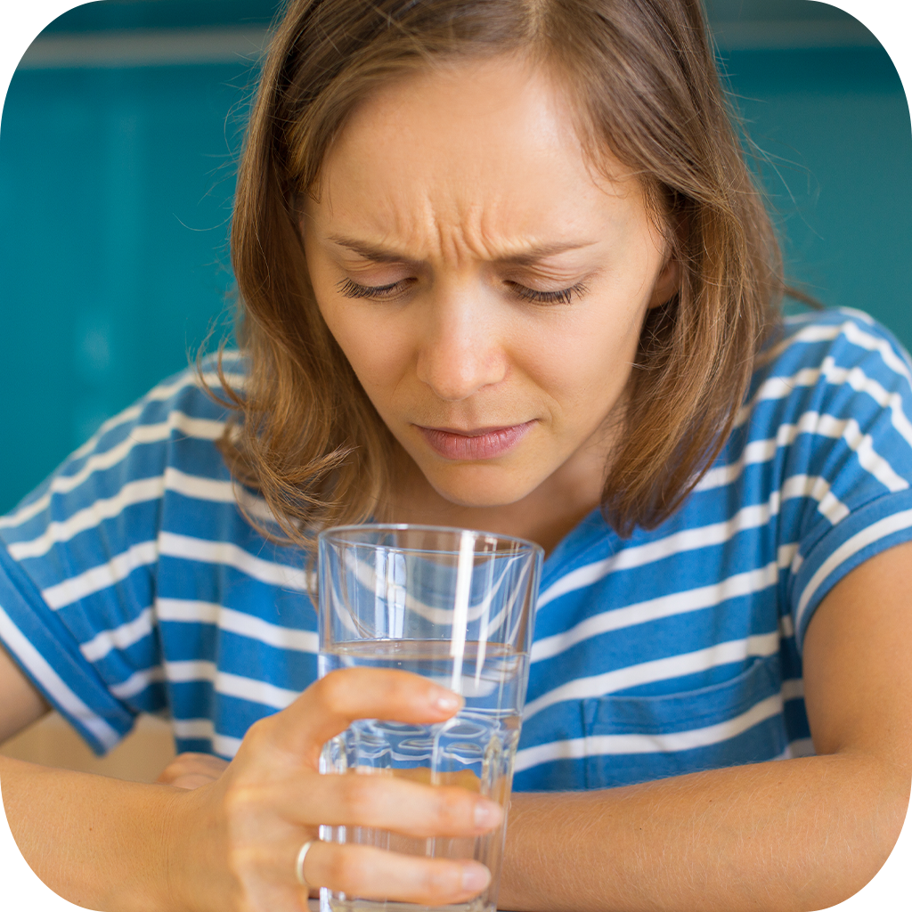 "A woman inspecting a glass of foul-smelling unfiltered tap water."