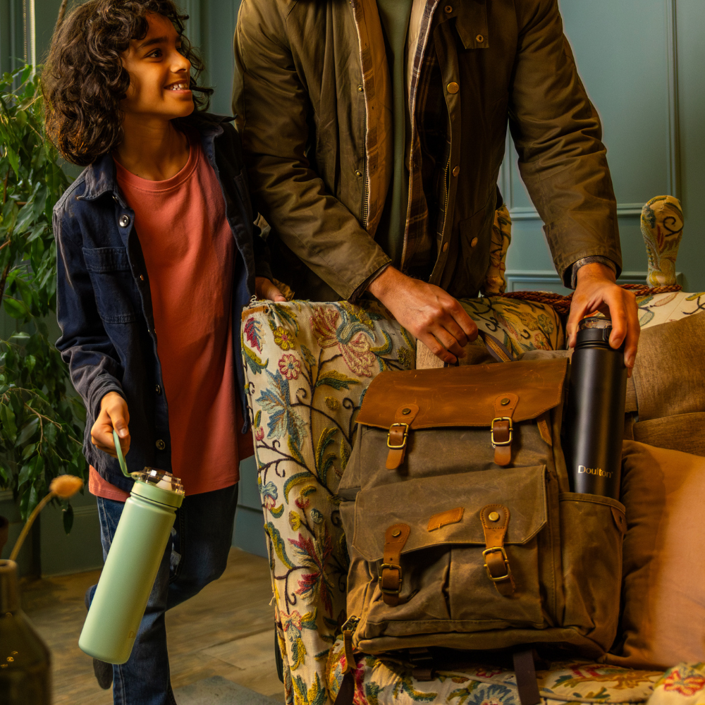 Two people with backpacks and water bottles on a floral-patterned chair.